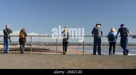 Menschen, die neben Geländern an der Strandpromenade bei Dawlish Warren stehen und über den Strand in Richtung Exmouth blicken. Stockfoto