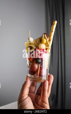 Man hält Jarcuterie in einem Glas, der modernen Version der Wurstwaren. Enthält verschiedene Arten von Wurst, Gurken und Käse Stockfoto