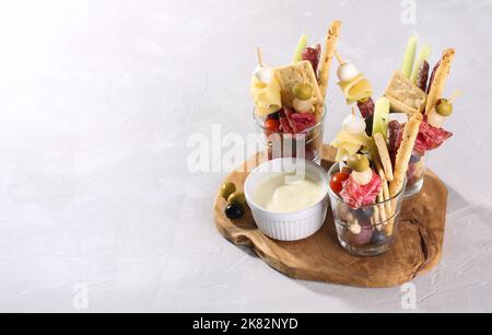 Jarcuterie in einem Glas, die moderne Version der Wurstwaren. Enthält verschiedene Arten von Wurst, Gurken und Käse, grauer Hintergrund Stockfoto