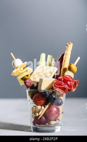 Jarcuterie in einem Glas, die moderne Version der Wurstwaren. Enthält verschiedene Arten von Wurst, Gurken und Käse, grauer Hintergrund Stockfoto