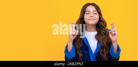 Abergläubisches Mädchen mit geschlossenen Augen halten die Daumen für Glück gelben Hintergrund gekreuzt, Wunsch. Kindergesicht, horizontales Poster, Teenager-Mädchen isoliert Stockfoto