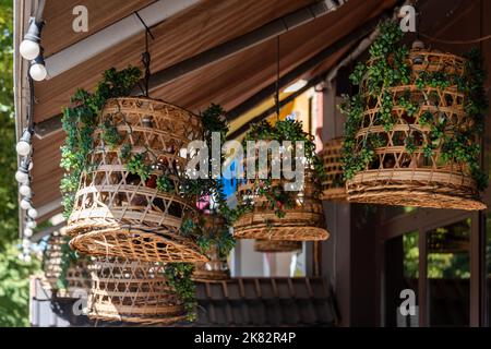 Korblampenschirme in einem Straßencafé im Freien. Dekorieren von hängenden Laternen-Lampen in hölzernen Korbkörben aus Bambus. Vintage asiatische Restaurant Dekorationen. Stockfoto