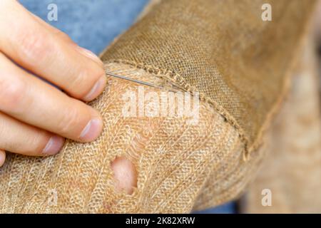 Hände Männer Nahaufnahme. Kleidung ausbessern, nähen und verfärben sowie modische Nadelarbeit. Selektiver Fokus Stockfoto