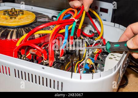 Reparatur des Spannungsstabilisators. Ein Elektriker entschrauben die Stromkabel des Stabilisators. Stockfoto