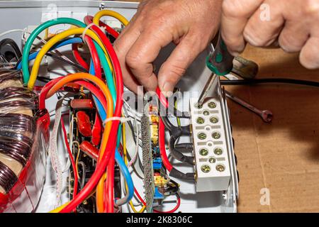 Reparatur des Spannungsstabilisators. Ein Elektriker entschrauben die Stromkabel des Stabilisators. Stockfoto