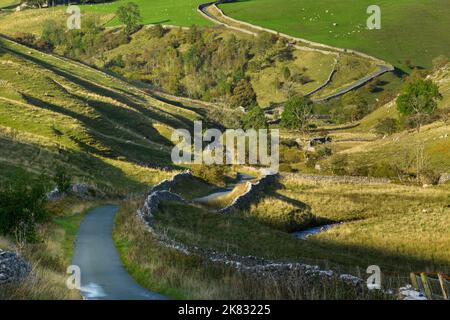 Ruhige, gewellte Landstraße (Talseiten, malerische sonnenbeschienenen Landschaften, steiler Aufstieg, Bach) - in der Nähe von Kettlewell, Yorkshire Dales, England, Großbritannien. Stockfoto