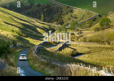 1 Auto auf einer ruhigen gewellten Landstraße (malerische, sonnendurchflutete, hügelige Landschaft, steiler Anstieg, Bach) - in der Nähe von Kettlewell, Yorkshire Dales, England. Stockfoto