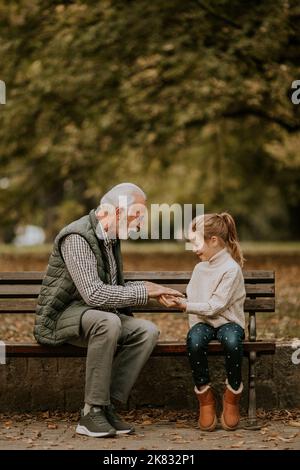 Der gutaussehende Großvater spielt am Herbsttag im Park mit seiner Enkelin ein Spiel mit roten Händen Stockfoto