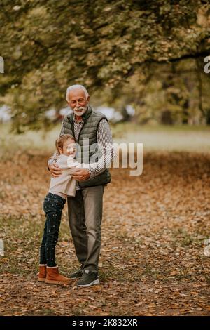 Der gutaussehende Großvater verbringt am Herbsttag Zeit mit seiner Enkelin im Park Stockfoto