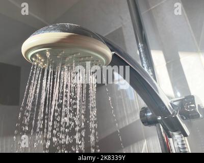 Nahaufnahme eines Duschkopfes mit der Sonne, die auf die fließenden Wassertropfen fällt. Wassersparender Duschkopf. Stockfoto