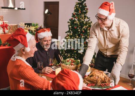 Frohe Weihnachten! Glückliche Familie essen zu Hause zu Abend. Feiertag und Zweisamkeit in der Nähe von Baum Stockfoto