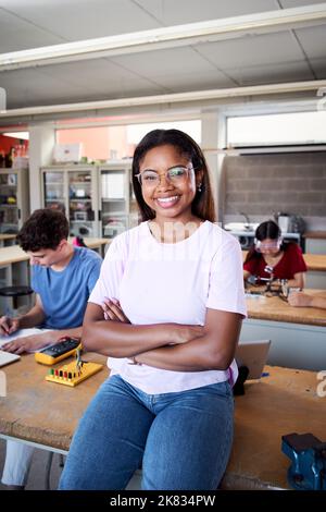 Vertikales Porträt eines Mädchens, das in einer Technologieklasse steht und die Kamera anschaut. Berufsschüler im Klassenzimmer studieren Elektronik Stockfoto