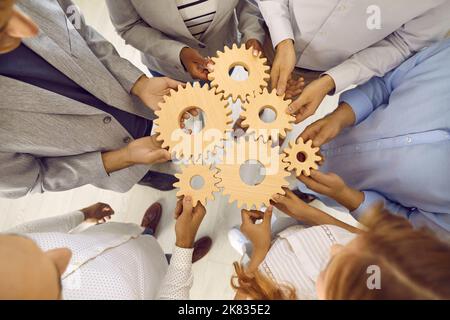 Hölzerne Zahnräder in verschiedenen Größen befinden sich in den Händen von Männern und Frauen, die sie mit dem Stapel verbinden. Stockfoto