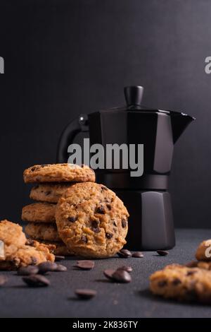 Hausgemachte leckere Schokoladenkekse mit schwarzer Geysir-Kaffeemaschine auf dunklem Beton-Hintergrund Stockfoto
