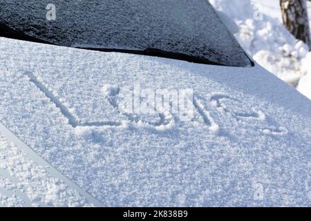 Die Inschrift auf der schneebedeckten Motorhaube des Autos in großen Buchstaben Liebe an einem sonnigen Wintertag. Selektiver Fokus. Nahaufnahme Stockfoto