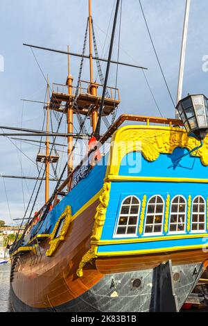 Blick auf das farbenfrohe Heck einer Nachbildung der HMS Endeavour aus dem 18.. Jahrhundert. Die Masten reichen bis zu einem wolkigen Himmel. Stockfoto