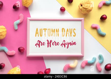 Text die Herbsttage sind wieder in rosa Rahmen. Verschiedene Süßigkeiten, Süßwaren und Preiselbeeren auf mehrlagigen farbigen Papier. Flach liegend, Draufsicht. Stockfoto