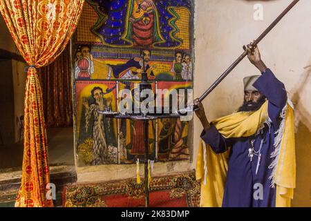 AXUM, ÄTHIOPIEN - 19. MÄRZ 2019: Priester zeigt farbenfrohe Gemälde in der Alten Kirche der heiligen Maria von Zion in Axum, Äthiopien Stockfoto