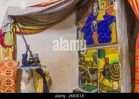 AXUM, ÄTHIOPIEN - 19. MÄRZ 2019: Priester zeigt farbenfrohe Gemälde in der Alten Kirche der heiligen Maria von Zion in Axum, Äthiopien Stockfoto