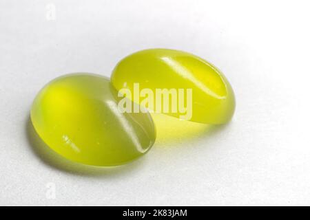 Zwei Peridots übereinander auf weißem Hintergrund. Ovaler Peridot-Cabochon mit Olivin-Schliff. Stockfoto