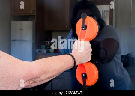 Frau, die einen Saugheber verwendet, um einen alten Spritzwasserrückstand aus gehärtetem Glas hinter einem Herd zu entfernen. Stockfoto