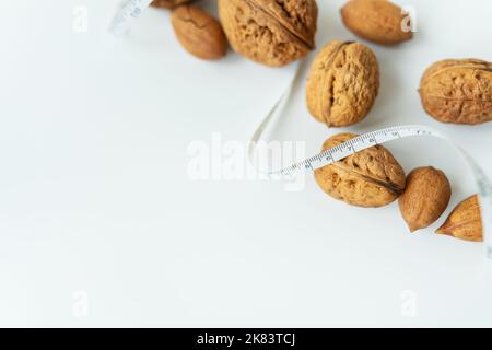 Schöne ganze Walnusskerne liegen zusammen mit einem kleinen Zentimeter, ganze Nüsse in der Schale werden auf dem Tisch verschüttet. Selektiver Fokus, Rauschen. Stockfoto