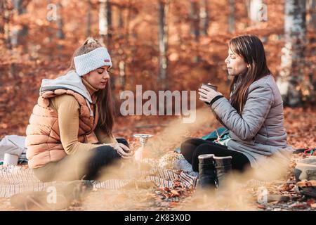 Zwei Mädchen trinken heißen Tee aus Metallbechern im Freien, Camping Stockfoto