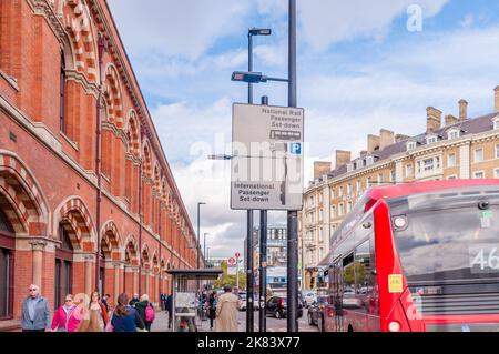 Personen und Gepäck, die auf einem Gehweg östlich des St Pancras International laufen, von der Pancras Road aus gesehen, die es von der King's Cross Station trennt Stockfoto