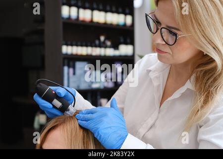 Doktor untersucht die Kopfhaut eines jungen Mädchens mit speziellen Dermatologie-Ausrüstung System, Haarausfall und Trichologie-Konzept Frau Haaranalyse mit Stockfoto