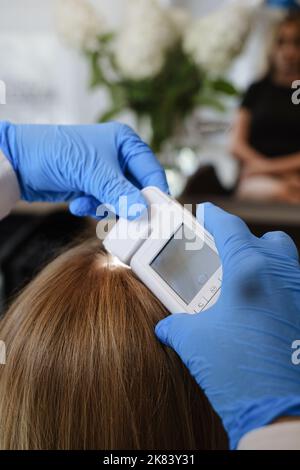 Doktor untersucht die Kopfhaut eines jungen Mädchens mit speziellen Dermatologie-Ausrüstung System, Haarausfall und Trichologie-Konzept Frau Haaranalyse mit Stockfoto