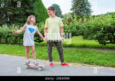 Glückliche Kinder reiten im Park auf einem Skateboard. Das Mädchen reitet an Bord Stockfoto