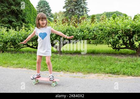 Ein kleines Mädchen lernt im Park ein Skateboard zu fahren. Gesunder Lebensstil Stockfoto