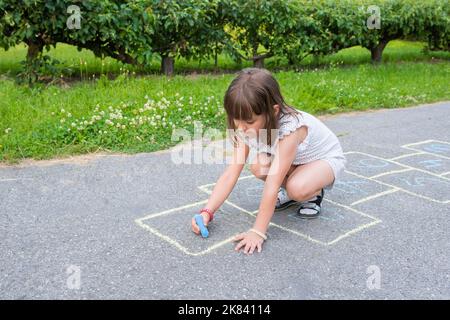 Ein kleines niedliches Schulmädchen zeichnet eine bunte Kreide auf den Bürgersteig Stockfoto