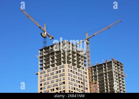 Turmkräne und unfertige Gebäude auf dem Hintergrund des blauen Himmels. Wohnungsbau, Wohnblocks in der Stadt Stockfoto