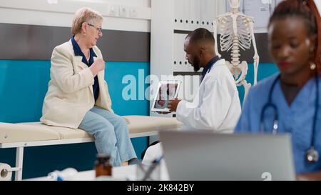 Kardiologischer Arzt, der eine kardiologische Diagnose auf einem digitalen Tablet bei einer kranken Frau mit Herzerkrankungen zeigt. Blick auf Herz-Kreislauf-ekg und Herzorgan auf dem Display, um medizinische Behandlung zu finden. Stockfoto