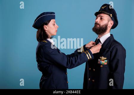 Flugbegleiter Befestigung Flieger Krawatte, Stewardess und Flugzeug Kapitän Paar in professionellen Uniform Porträt, Studio Medium Shot. Selbstbewusste Flugzeugbesatzung, Flieger und Flugbegleiterin Stockfoto