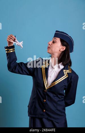 Flugbegleiter in Uniform halten Flugzeugmodell, Luftfahrt-Akademie Stewardess spielt mit Flugzeug. Lufthostess, die kommerzielle Jet-Spielzeug, Seitenansicht Studio mittlere Aufnahme Stockfoto