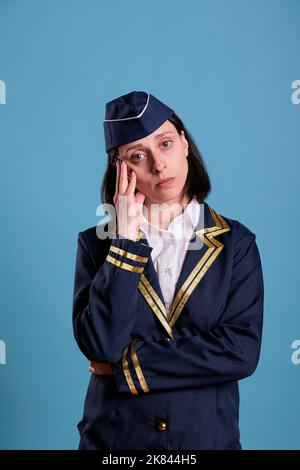 Erschöpfte Stewardess, die an Migräne leidet, Kopfschmerzen hat, Schläfen mit dem Finger berührt, während sie auf die Kamera schaut. Flugbegleiter in Uniform fühlt sich unwohl, erschöpfte Flugbegleiterin Stockfoto