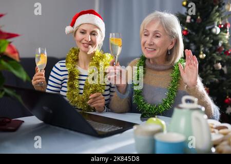 Glückliche Erwachsene Tochter und ältere Mutter mit Cocktails in den Händen wünschen Verwandten frohe Weihnachten über das Internet Stockfoto