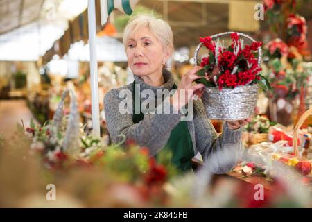 Ältere Verkäuferin, die Weihnachtsdekoration in den Regalen des Ladens arrangiert Stockfoto