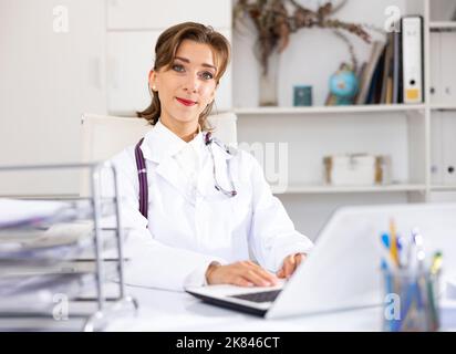Porträt einer lächelnden Ärztin, die im Büro einen Laptop benutzt Stockfoto