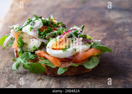 Offenes Sandwich mit geräuchertem Lachs, Ei, eingelegten Zwiebeln, Sauerrahm und Kapern Stockfoto