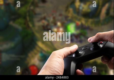 Ein modernes GAM22ICB Gamepad in den Händen eines Spielers vor dem Hintergrund eines hellen Abenteuerspiels auf dem Bildschirm eines großen Plasmafernsehers. Online-Spiele w Stockfoto