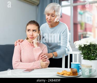 Ältere Frau beruhigt geächtete Erwachsene Tochter am Tisch Stockfoto