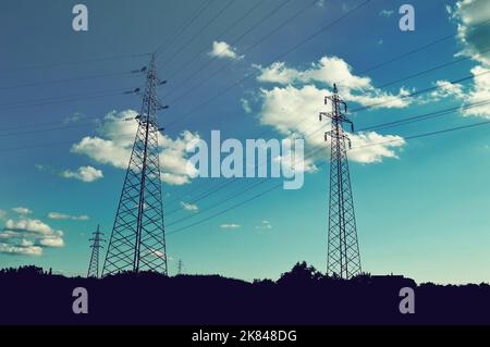 Sendetürme mit Hochspannungsleitungen. Silhouetten von Strommasten auf dem Feld Stockfoto