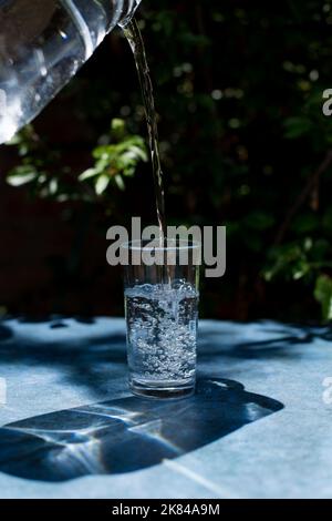 Wasser in einen Glasbecher gießen. Konzept der gesunden Getränke. Stockfoto