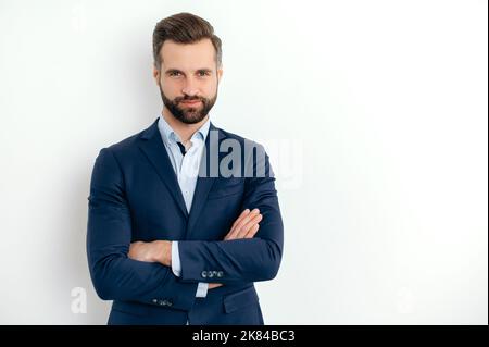 Charismatische attraktive positive kaukasische erfolgreiche bärtige Mann in einem Anzug, Geschäftsmann, seo, stehend über isolierten weißen Hintergrund mit gekreuzten Armen, Blick auf die Kamera, lächelnd Stockfoto