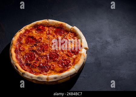 Pizza mit Tomatensauce, Mozzarella, Salami, Chili, Honig auf schwarzem Hintergrund. Blick von oben. Stockfoto