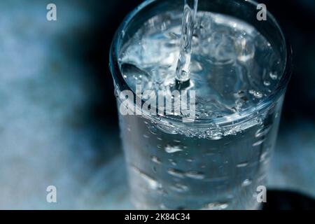 Wasser in einen Glasbecher gießen. Konzept der gesunden Getränke. Stockfoto