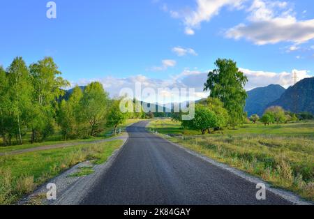 Eine Straße in einem Bergtal. Eine grüne Wiese am Fuße des Altai-Gebirges unter einem wolkenblauen Himmel. Altai-Republik, Sibirien, Russland, 2022 Stockfoto